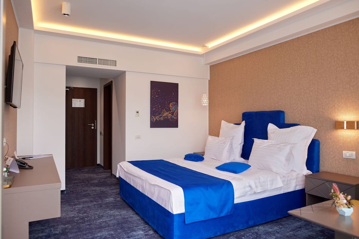 A hotel room with a large bed, a desk, a television, and a wall-mounted light fixture.