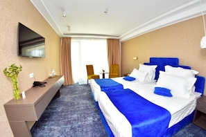 A hotel room with two beds, a desk, a TV, and a window with curtains. - Stavros (Navodari)