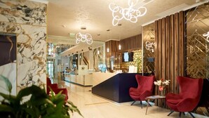 Un hall d'hotel modern amb una recepció, cadires vermelles i una paret de marbre.