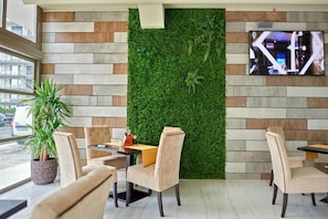 A modern cafe with a green wall, comfortable seating, and a TV screen. - Stavros (Navodari)