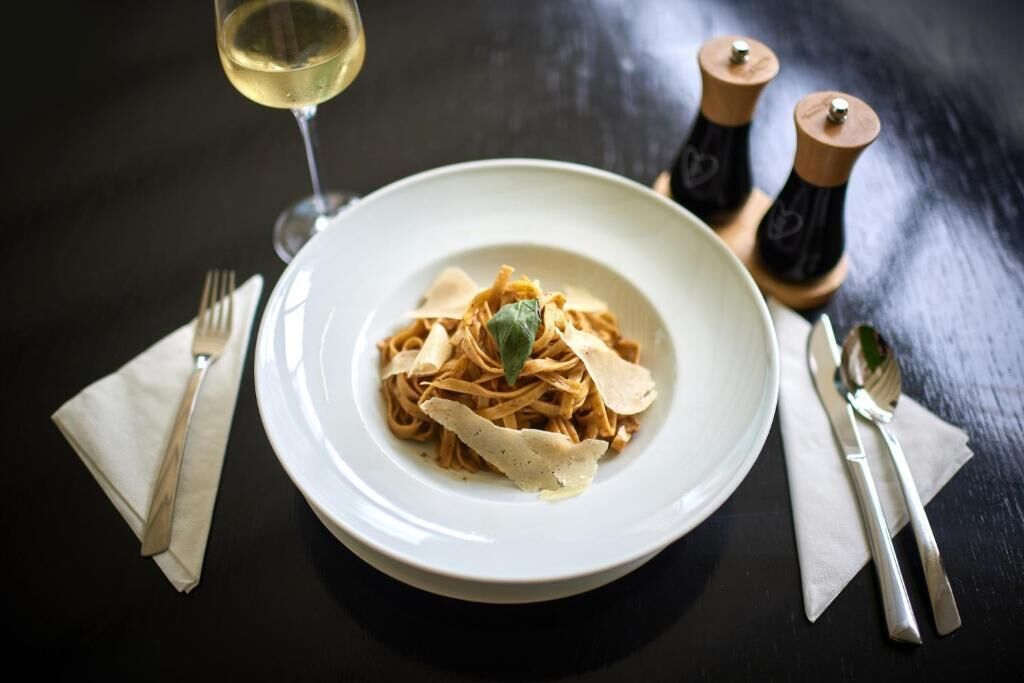 A plate of pasta with a glass of white wine on a dark table.