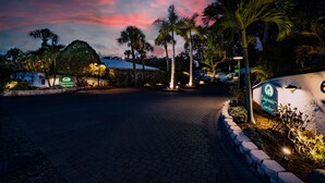 Vue nocturne d’un jardin, avec un panneau indiquant « Jardin polynésien » et un chemin pavé.