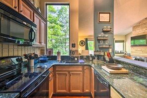 Una cocina moderna con encimeras de granito, electrodomésticos de acero inoxidable, armarios de madera y un amplio ventanal con vistas a zonas verdes.