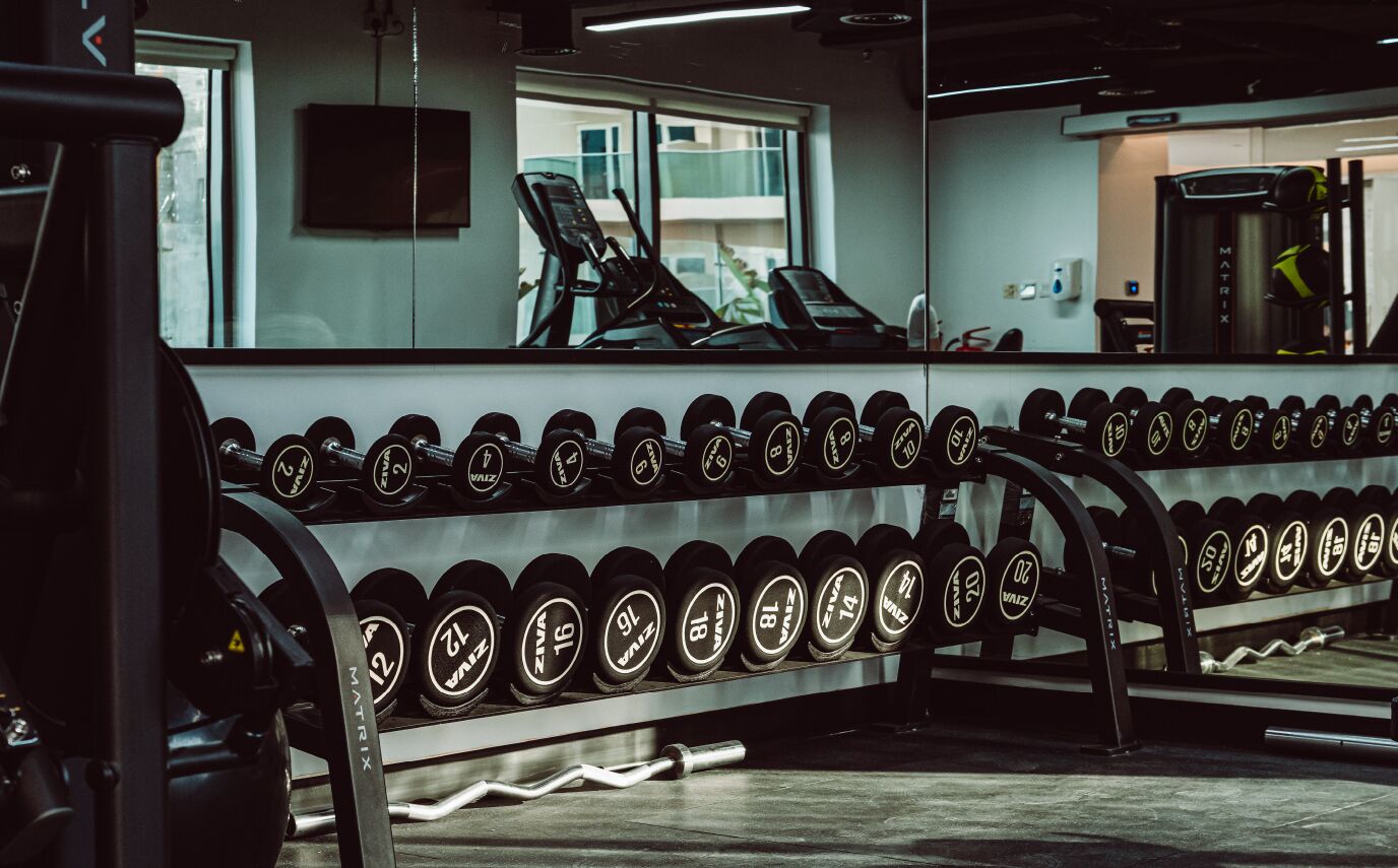 Un gimnasio con un espejo que refleja equipos de ejercicio y un ventanal con vistas a edificios.