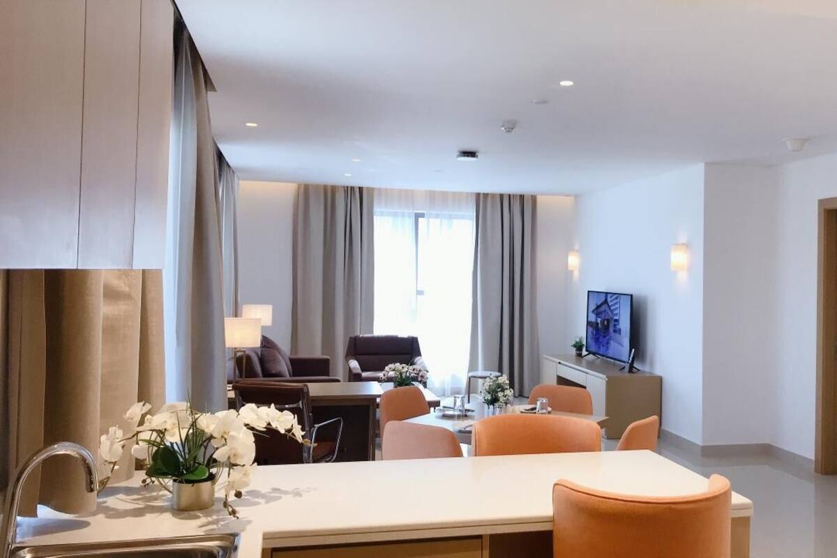 Habitación de hotel moderna con comedor, sofá, televisor y un amplio ventanal con cortinas.
