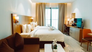 Een hotelkamer met een groot bed, een bureau met een computer, een bank en een kleine tafel met een plant.