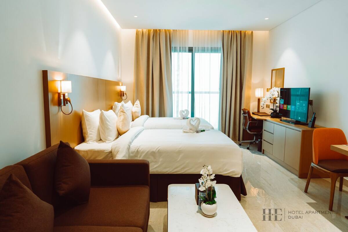 Una habitación de hotel con una cama grande, un escritorio con computadora, un sofá y una pequeña mesa con una planta.