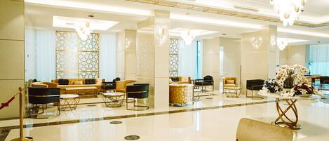 Um hall amplo com design moderno, com área de estar com sofás e poltronas, parede decorativa com padrões geométricos e um lustre.