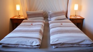 A twin bed with striped bedding, two bedside tables with lamps, and a sheer curtain.
