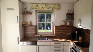 A compact kitchen with white cabinets, a wooden countertop, a built-in oven, and a window with a lemon-patterned valance.