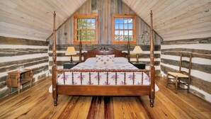 A log cabin bedroom with a four-poster bed, two windows, and wooden floors.