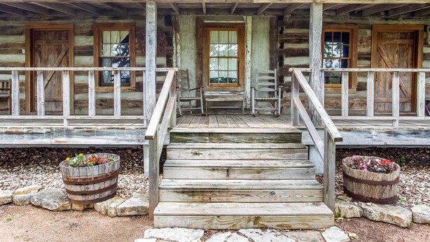 A wooden cabin with a front porch, a set of wooden stairs, and two flower pots.