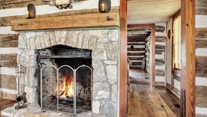 A stone fireplace with a metal screen, wooden logs, and a lit fire.