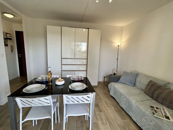 A modern living room with a sofa, a dining table with chairs, and a kitchen area with cabinets.
