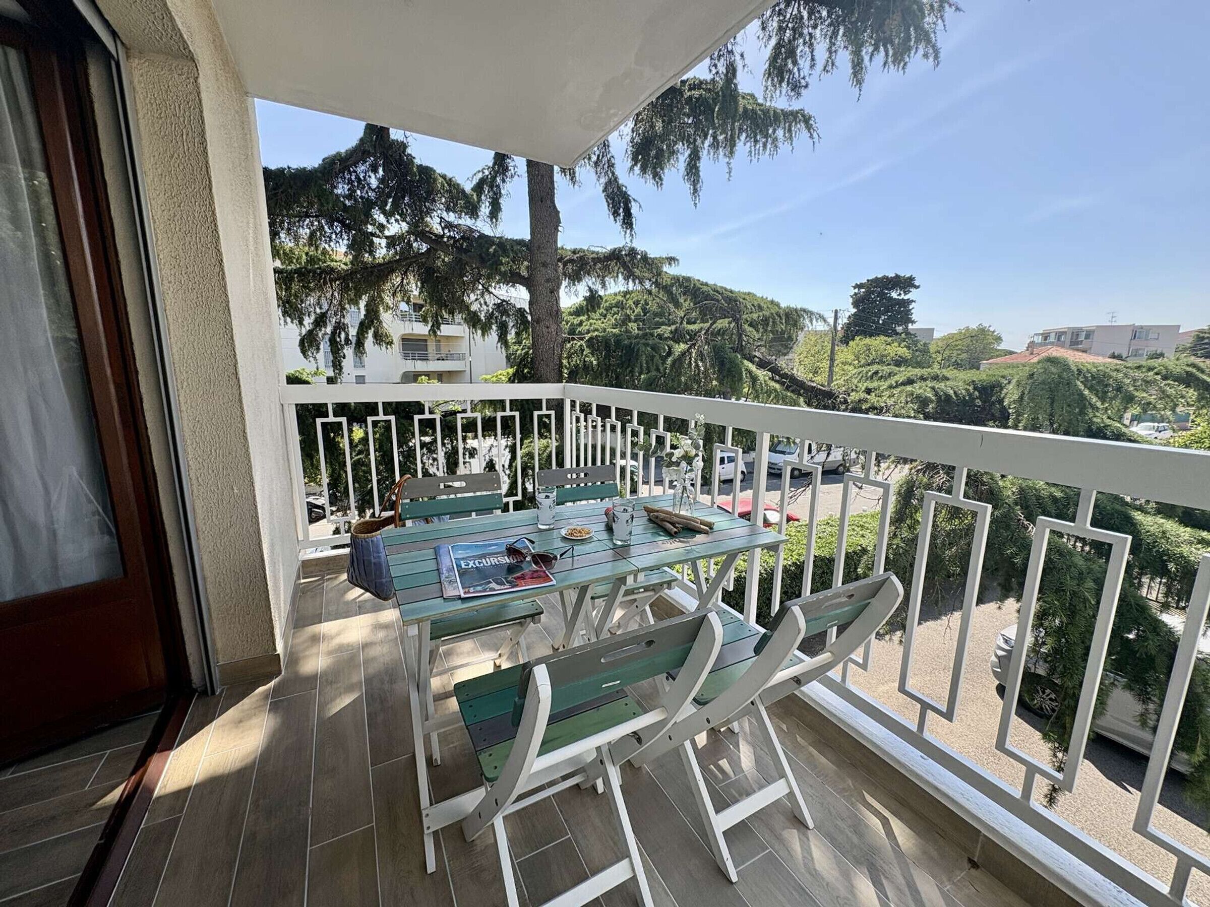 A balcony with a table and chairs, a view of the surrounding area, and a building in the background.