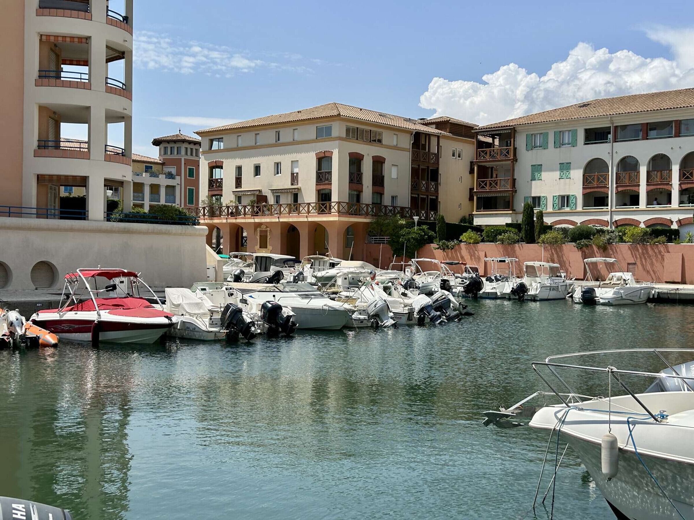 A marina with several boats docked, surrounded by multi-story buildings with balconies.