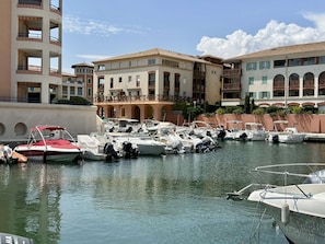 A marina with several boats docked, surrounded by multi-story buildings with balconies.