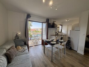 A compact living space with a sofa, dining table, chairs, a kitchen area, and a balcony with a view.