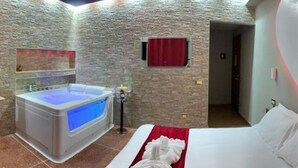 A hotel room with a stone-textured wall, a large bathtub with blue lighting, a bed with white linens, and a red curtain. - Cleopatra (Rome)