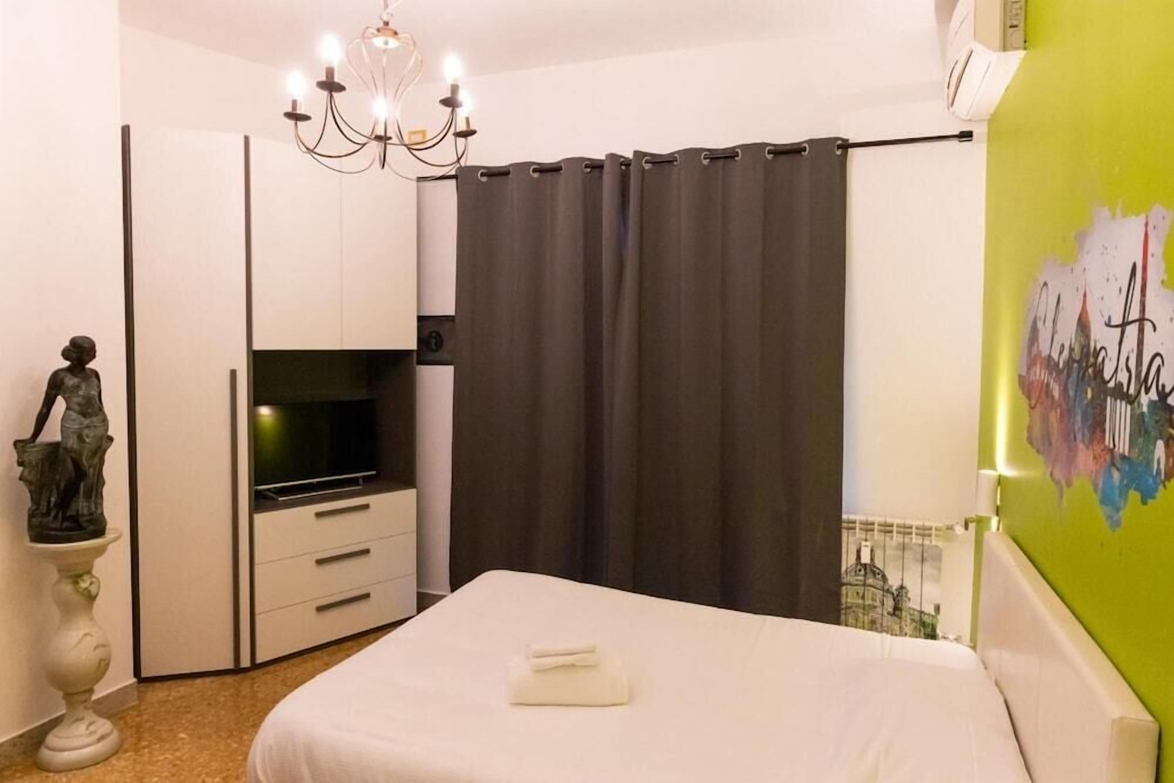 A hotel room with a bed, a television, a statue, a chandelier, and a curtain.
