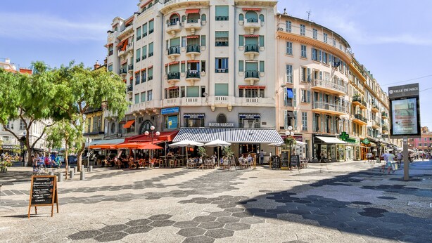 Ein mehrstöckiges Gebäude mit einer geschwungenen Fassade, Außenbereichen zum Verweilen und einem Schild für Maison Margaux.