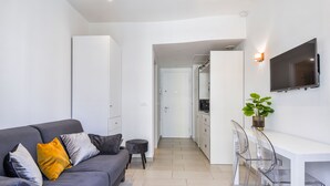 Ein modernes Wohnzimmer mit einem grauen Sofa, einem kleinen runden Tisch und einem an der Wand montierten Fernseher.