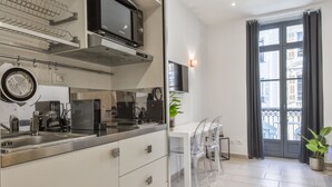 Eine moderne Küche mit Edelstahlgeräten, ein Essbereich mit transparenten Stühlen und ein Balkon mit Blick auf Gebäude.