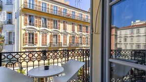 Ein Balkon mit weißen Stühlen und einem kleinen Tisch, mit Blick auf eine Reihe bunter Häuser mit Balkonen.