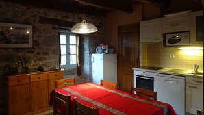 Una cocina acogedora con mantel rojo, armarios de madera, un refrigerador, un microondas y una lámpara colgante.