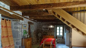 Una habitación rústica con techo de madera, paredes de piedra, una mesa de madera con mantel rojo y una escalera.