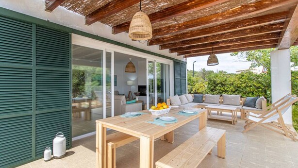 Une terrasse extérieure avec une table en bois, des bancs et un espace salon agrémenté de coussins.