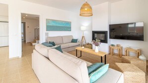 Un salon moderne avec un canapé beige, une table basse en bois, une lampe et un téléviseur.