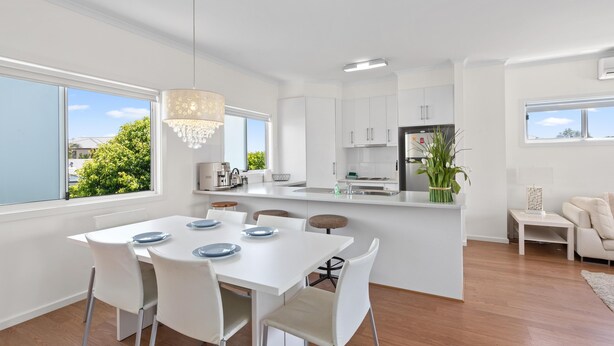 Een moderne keuken met witte kasten, een eethoek met witte stoelen en uitzicht op groen.