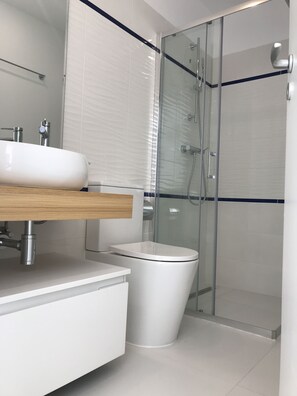 Uma casa de banho moderna com chuveiro em cabine de vidro, lavatório branco e sanita.