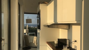 A modern kitchen with a view of the sea, a small dining area, and a balcony with a statue.