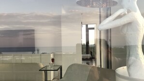 A modern living room with a sofa, a glass coffee table, and a large window overlooking a beach.