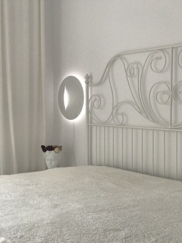 A white bed with a headboard featuring a circular mirror and a small vase with dried flowers.