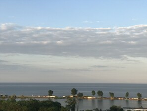 Vista costeira com mar calmo, céu claro e uma linha de árvores e edifícios ao longo da praia.