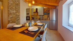 Un comedor con una mesa de madera dispuesta para dos personas, una pared de piedra y una cocina al fondo.