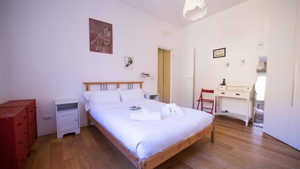 Ein Schlafzimmer mit einem hölzernen Bett, weißer Bettwäsche, einem Schreibtisch und einem Stuhl.