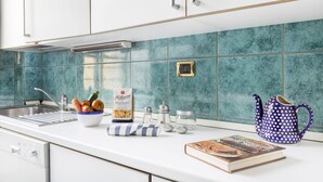 A kitchen with white cabinets, a teal backsplash, a sink, a bowl of vegetables, a cookbook, and a polka-dotted teapot. - GetTheKey appartamento Quadrilatero (Bologna)