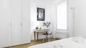 A hotel room with a bed, a desk with a chair, a radiator, and a poster on the wall. - GetTheKey San Vitale Apartment (Bologna)