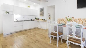 A modern kitchen with white cabinets, a wooden floor, and a dining area with white chairs and a table. - GetTheKey San Vitale Apartment (Bologna)