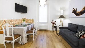 A dining area with a table set for four, a sofa, a TV mounted on the wall, and a window with natural light. - GetTheKey San Vitale Apartment (Bologna)