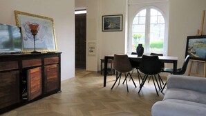 A living room with a wooden herringbone floor, a grey sofa, a dining area with a table and chairs, and artwork on the walls. - Renovated house 100m from sea with WIFI, garden in Trégastel (Trégastel)