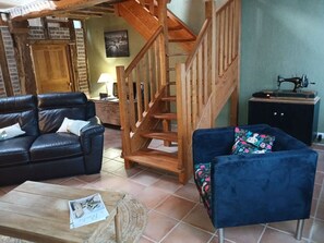 A rustic interior with a wooden staircase, leather sofas, a small table with a newspaper, and a vintage sewing machine.