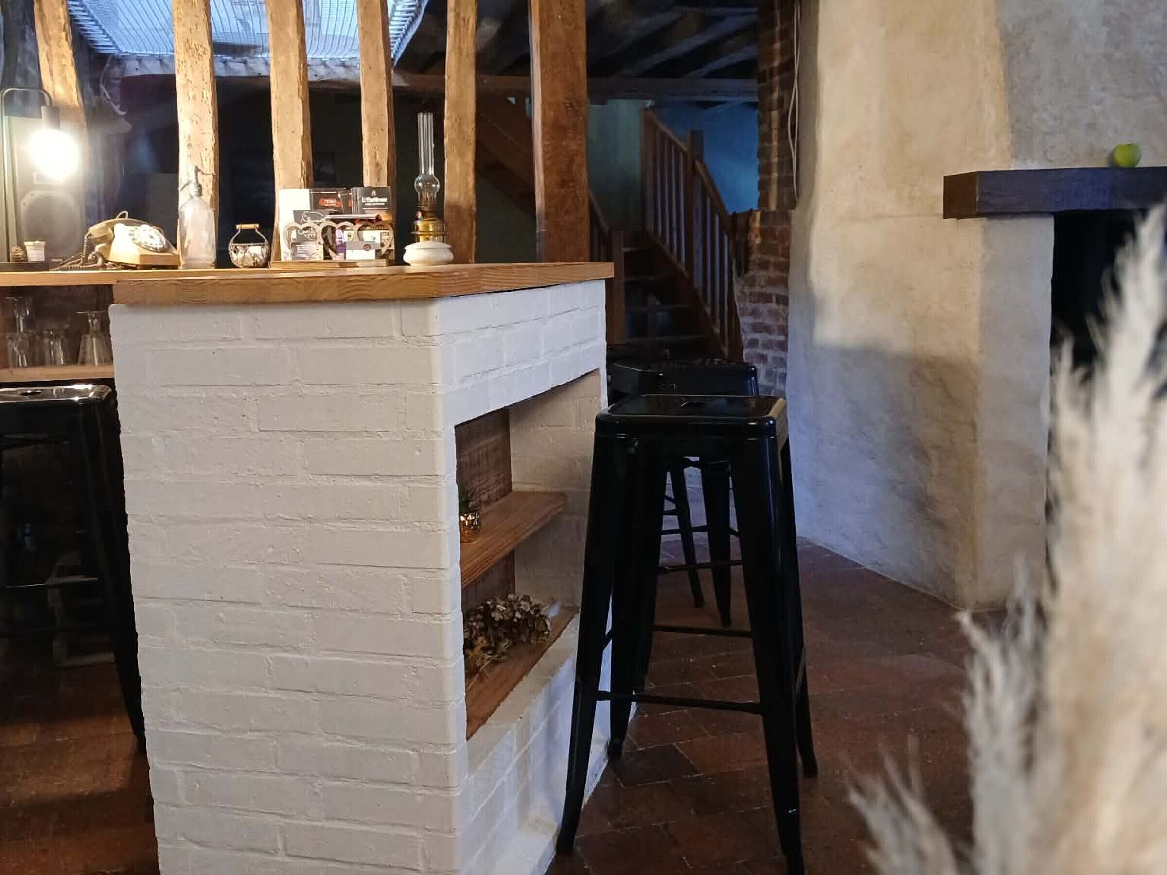 A rustic interior with a brick fireplace, wooden beams, a bar area with a telephone, and a staircase leading to an upper level.