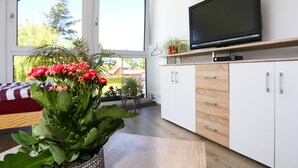 A modern living room with a large window, a flat-screen TV, and a wooden cabinet. - Große Ferienwohnung Mitten im Grünen (Ziesendorf)