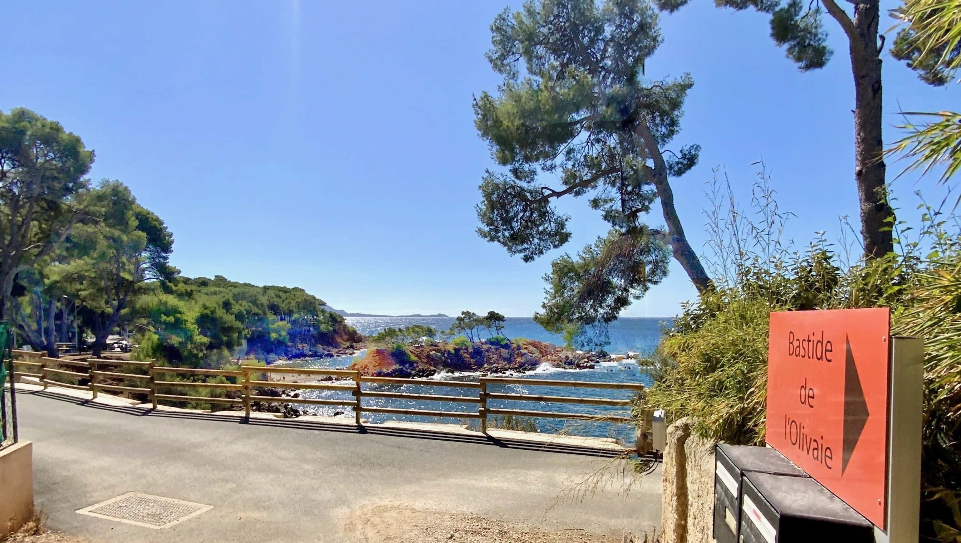 Una carretera costera con una valla de madera y un cartel que indica 'Bastide de l'Olivai'.