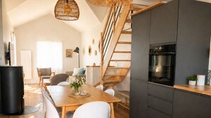 Eine moderne Küche mit einem schwarzen Kühlschrank, einem Holztisch, weißen Stühlen und einer Holztreppe.